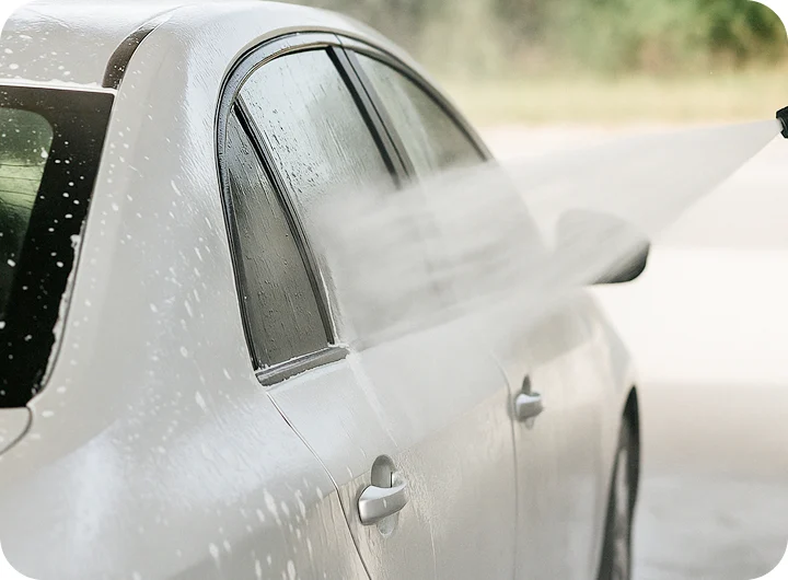 threeColumnsDetails__list__item__image 白い車の側面を高圧洗浄で洗浄する作業