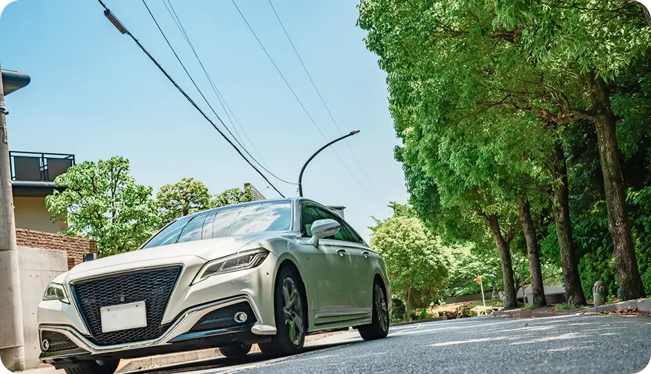 住宅街の並木道を走る白いセダン